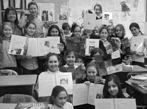 Smiling Grannie Annie students in New York hold up the stories they wrote about their family's history.